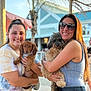 Piper is registered to the contest to win money with this photo: woman, dog, puppy, smile, sunglasses, outdoor, daylight, casual, tie_dye, jeans, tattoo, beach, palm_tree, building, leash, summer, friendship, portrait, happy, holding