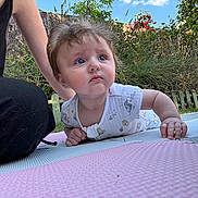 Penelope is registered to the contest to win money with this photo: baby, child, infant, outdoor, garden, grass, picket_fence, greenery, mat, playing, curious, blue_eyes, onesie, person, adult, casual_clothing, sunny, daylight, nature, candid