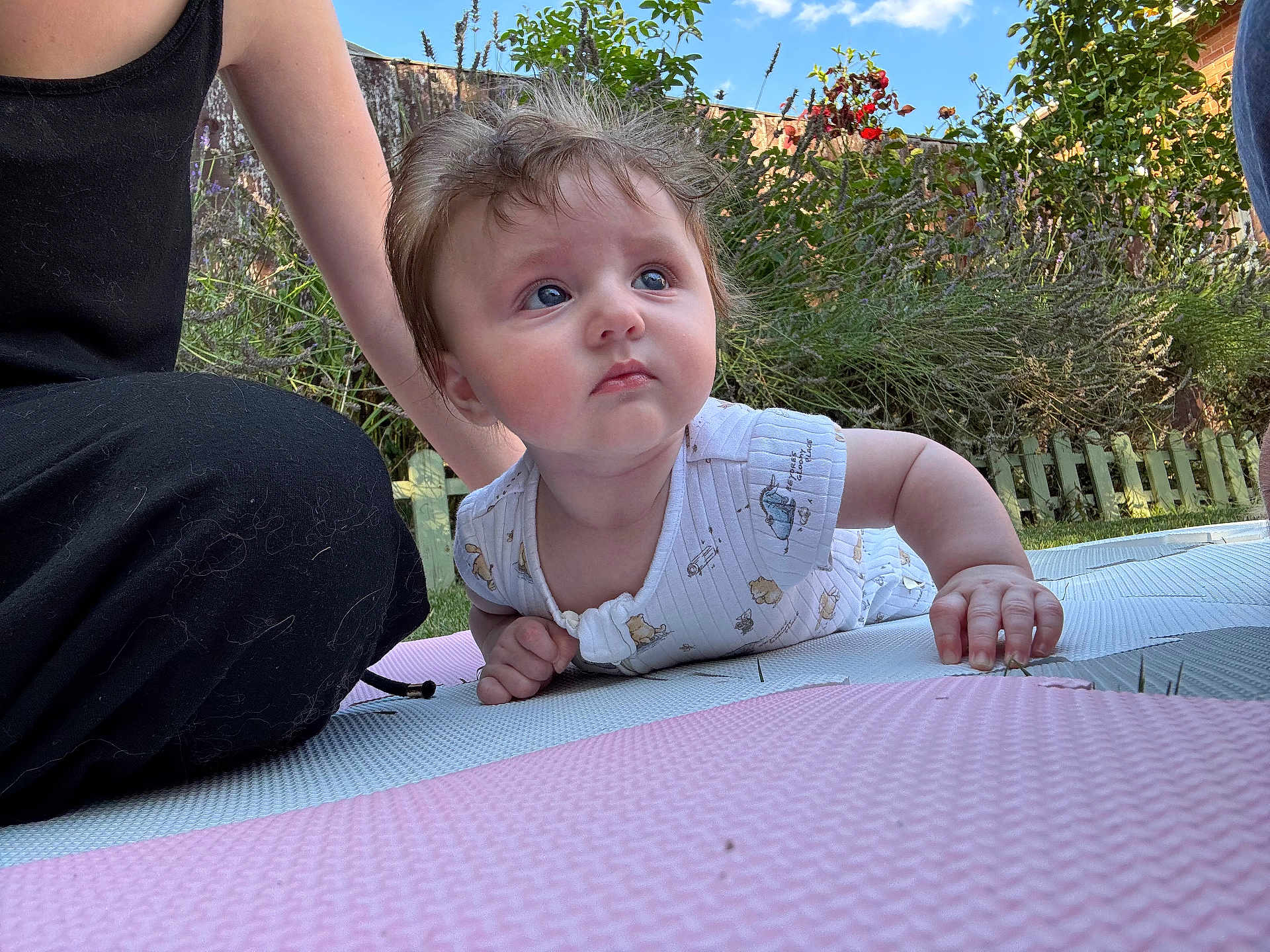 Penelope is registered to the contest to win money with this photo: baby, child, infant, outdoor, garden, grass, picket_fence, greenery, mat, playing, curious, blue_eyes, onesie, person, adult, casual_clothing, sunny, daylight, nature, candid