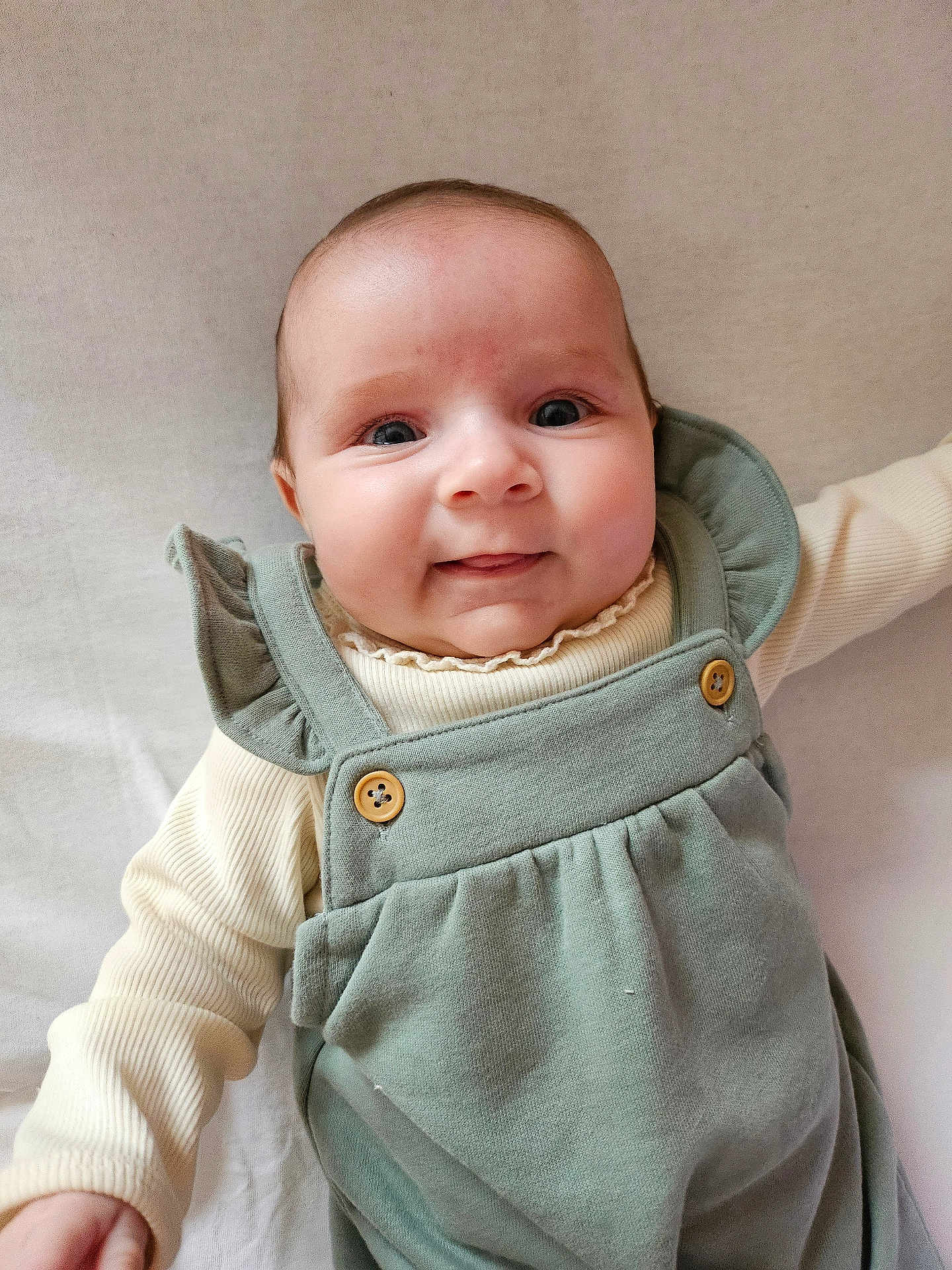 Jade participe au concours pour gagner de l'argent avec cette photo : baby, infant, child, smiling, face, eyes, clothing, green_outfit, buttons, cute, portrait, indoor, neutral_background, soft_lighting, person, young_child, baby_girl, baby_boy, happy, closeup