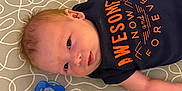 Gary is registered to the contest to win money with this photo: baby, infant, onesie, pacifier, crib, mattress, pattern, blue, orange, lying_down, small_hands, cute, child, face, skin, head, sleeping_area, soft, newborn, indoors