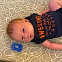 baby, infant, onesie, pacifier, crib, mattress, pattern, blue, orange, lying_down, small_hands, cute, child, face, skin, head, sleeping_area, soft, newborn, indoors