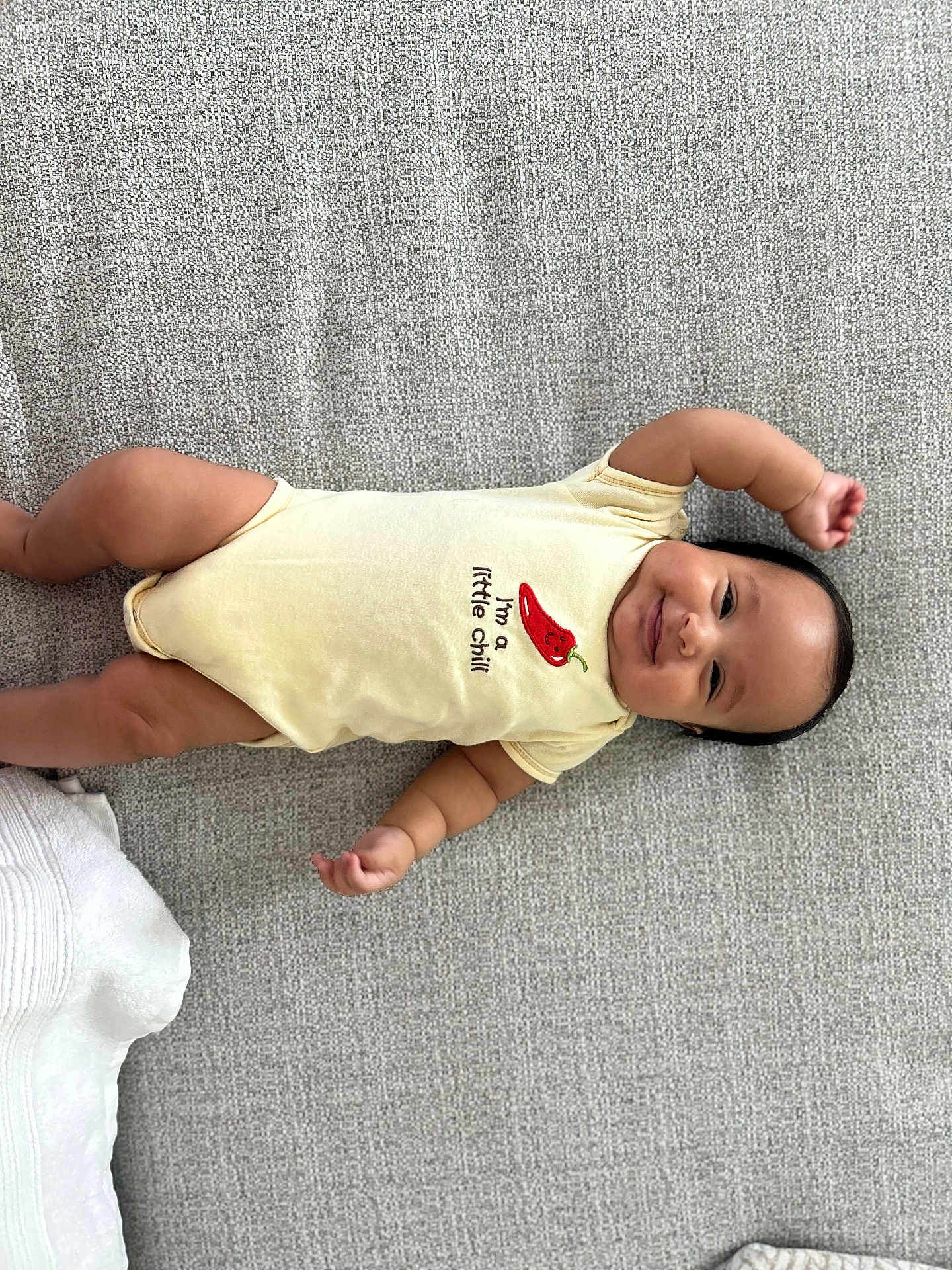 Benjamin joined the competition — help win amazing prizes! baby, infant, smiling, lying_down, onesie, yellow_clothing, chili_pepper_graphic, cute, happy, child, arm_raised, cheeks, face, skin, person, indoor, textile_background, soft_texture, playful, young