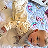 Ivy is registered to the contest to win money with this photo: baby, child, smiling, pajamas, quilt, blanket, indoor, face, happy, infant, clothing, colorful, pattern, soft, cute, lying_down, person, playful, pastel, bib