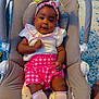 baby, baby_rocker, banana_toy, bird_toy, blue_rug, carrying_handle, child, cushion, cute, headband, indoor, infant, person, pink_shorts, portrait, relaxing, smiling, socks, toy, white_top