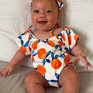Zaaryah joined the competition — help win amazing prizes! baby, child, smiling, headband, orange_pattern, blue_leaves, outdoor, cute, happy, infant, sitting, pillow, bed, foot, toes, clothing, person, portrait, skin, face