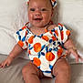 baby, child, smiling, headband, orange_pattern, blue_leaves, outdoor, cute, happy, infant, sitting, pillow, bed, foot, toes, clothing, person, portrait, skin, face