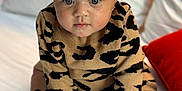 Zaaryah is registered to the contest to win money with this photo: baby, infant, child, face, curly_hair, sweater, leopard_print, black_booties, hands, feet, bed, white_bed, pillow, cushion, indoor, portrait, cute, curious, sitting, young_child