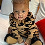 baby, infant, child, face, curly_hair, sweater, leopard_print, black_booties, hands, feet, bed, white_bed, pillow, cushion, indoor, portrait, cute, curious, sitting, young_child