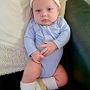Ghilés a rejoint le concours — aidez-le/la à gagner de superbes lots ! baby, infant, blue_onesie, knit_hat, socks, shoes, couch, pillow, blanket, hands, feet, face, eyes, indoor, portrait, cute, child, soft_lighting, relaxing, cozy
