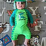 baby, child, dinosaur_outfit, green_clothing, play_mat, animal_illustrations, colorful, infant, cute, smiling, lying_down, indoors, headwear, hat, face, feet, hands, bright_colors, pattern, soft_surface