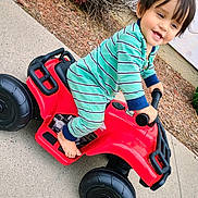 Mateo joined the competition — help win amazing prizes! toddler, child, toy_car, red, green_onesie, barefoot, smiling, outdoor, sidewalk, autumn_leaves, play, happy, young_child, person, plastic_toy, vehicle, casual_clothing, daylight, nature, fun