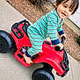 toddler, child, toy_car, red, green_onesie, barefoot, smiling, outdoor, sidewalk, autumn_leaves, play, happy, young_child, person, plastic_toy, vehicle, casual_clothing, daylight, nature, fun