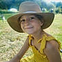 child, hat, yellow_dress, smile, outdoor, sunlight, grass, nature, bracelets, portrait, summer, happy, sitting, person, young_girl, fashion, casual, daytime, headwear, blurred_background