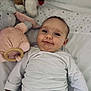 baby, infant, smile, white_shirt, denim_pants, plush_toy, stuffed_animal, bed, soft, cute, child, face, happy, lying_down, indoors, young, portrait, cozy, clothing, hand