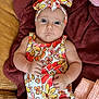 baby, infant, face, headband, floral_pattern, clothing, blanket, fabric, skin, hand, expression, indoor, comfort, couch, pink, orange, yellow, white, person, portrait