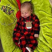 Paisley is registered to the contest to win money with this photo: baby, black_clothing, child, cozy, cute, footed_pajamas, green_blanket, grinch_face, holiday_theme, indoors, infant, onesie, peaceful, plush_blanket, portrait, red_clothing, reindeer_design, sleeping, soft_texture, wooden_floor