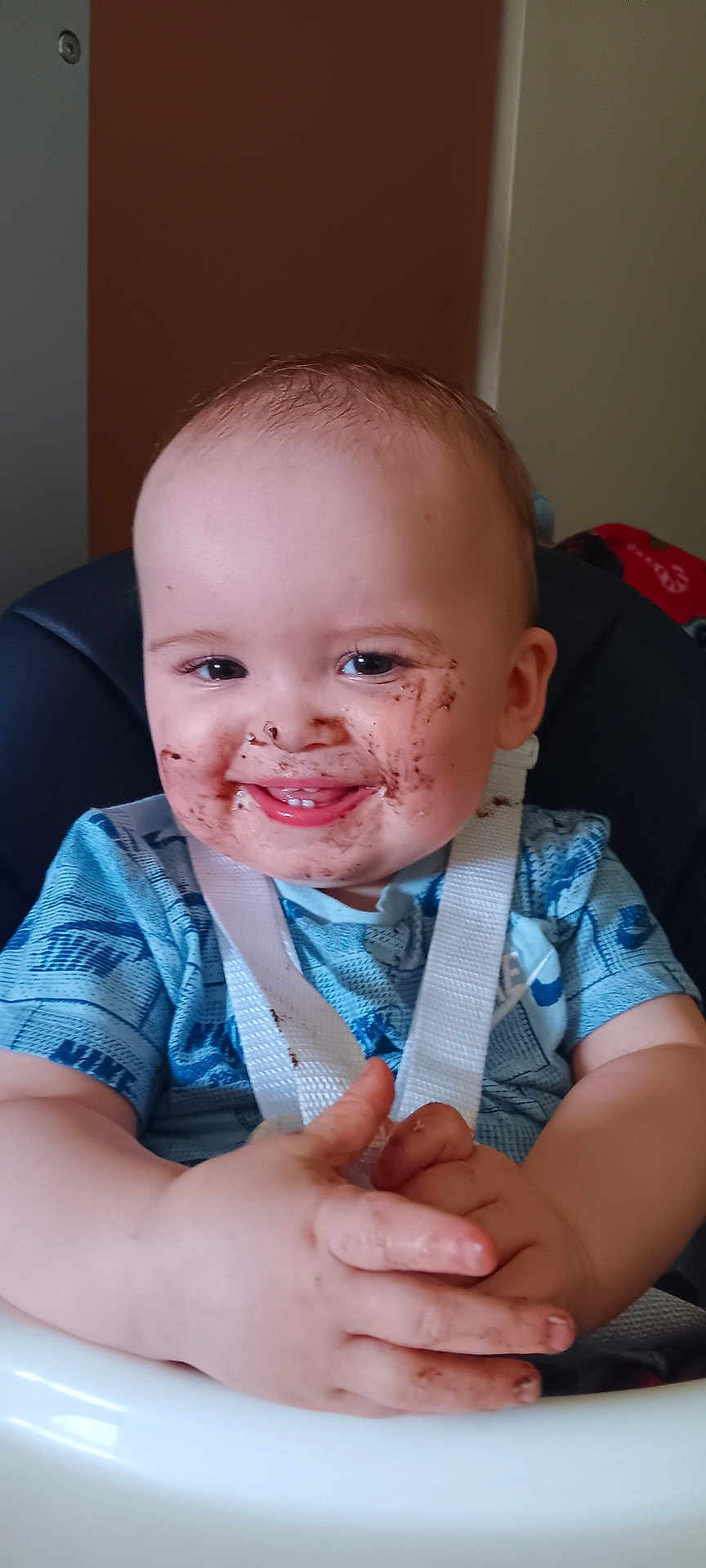 Reilly joined the competition — help win amazing prizes! baby, child, smiling, chocolate, face, hands, high_chair, blue_shirt, white_strap, happy, messy, indoor, person, infant, cute, young_child, seat, feeding_time, food, fun