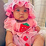 baby, infant, pink_clothing, strawberry, hat, cute, sitting, couch, indoors, child, portrait, chubby, feet, curious, soft_lighting, textile, fabric, cute_outfit, baby_fashion, relaxed