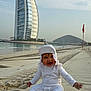 baby, beach, sand, smiling, child, sunhat, burj_al_arab, water, sky, sand_tracks, outdoor, happy, vacation, holiday, coast, footprints, person, clothing, tourist, seaside