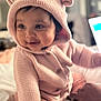 Liyana is registered to the contest to win money with this photo: baby, child, pink_hoodie, knitwear, cute, smiling, indoors, soft_light, bed, blanket, portrait, happy, face, sitting, infant, cozy, hood, cuddly, warm_clothing, person