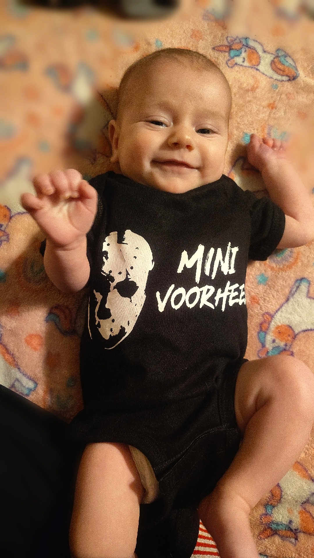 Ryan is registered to the contest to win money with this photo: baby, infant, smiling, onesie, black_clothing, unicorn_blanket, hand, face, cute, lying_down, child, happy, apparel, patterned_blanket, small_hand, baby_garment, infant_clothing, portrait, indoors, soft_texture