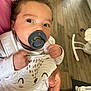 Marley participe au concours pour gagner de l'argent avec cette photo : baby, pacifier, infant, cute, hand, clothing, indoor, wooden_floor, person, child, white_outfit, smiling_face_design, holding, curious, closeup, human, newborn, comfort, soft_lighting, portrait