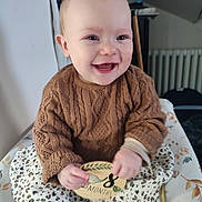 Elyna participe au concours pour gagner de l'argent avec cette photo : baby, child, smiling, knitted_sweater, brown_sweater, plaque, 8_months, patterned_skirt, blanket, indoor, happy, portrait, sitting, cozy, cute, infant, clothing, hands, face, young_child