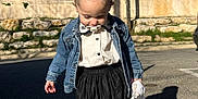 Romy a rejoint le concours — aidez-le/la à gagner de superbes lots ! toddler, child, denim_jacket, white_tights, black_skirt, white_shoes, pacifier, toy_blanket, outdoor, sunny, sidewalk, shadow, trees, fence, street, curb, casual_clothing, young_child, portrait, daytime