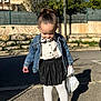 toddler, child, denim_jacket, white_tights, black_skirt, white_shoes, pacifier, toy_blanket, outdoor, sunny, sidewalk, shadow, trees, fence, street, curb, casual_clothing, young_child, portrait, daytime