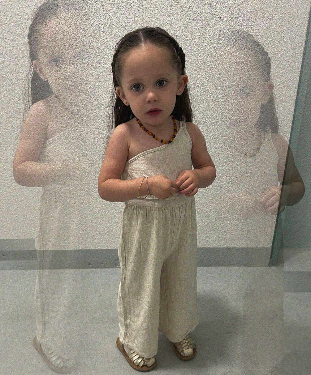 Romy participe au concours pour gagner de l'argent avec cette photo : child, girl, braids, standing, curious, neutral_colors, jumpsuit, sandals, floor, wall, reflection_effect, ghost_images, indoor, portrait, expression, young, person, fashion, accessories, bracelet