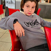 Cristian joined the competition — help win amazing prizes! child, person, red_chair, gray_sweater, headband, indoor, cafe, table, casual_clothing, modern_interior, relaxed_pose, young, face, seated, watch, black_jeans, lighting, blurred_background, portrait, confident