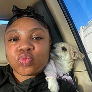 Queen joined the competition — help win amazing prizes! person, puppy, dog, selfie, close_up, car_interior, window, daylight, black_hoodie, headscarf, cute, affectionate, pet, animal, puckered_lips, small_dog, pink_outfit, snuggling, human_face, travel
