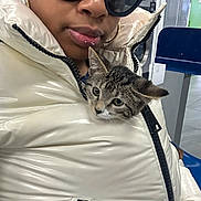 Joy is registered to the contest to win money with this photo: cat, kitten, puffer_jacket, zipper, sunglasses, lip_piercing, earing, laundromat, washer, dryer, indoor, seated, closeup, portrait, tabby, striped_fur, chair, tiled_floor, waiting_area, fashion