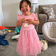 Jama Solana is registered to the contest to win money with this photo: child, girl, pink_dress, smiling, laughing, living_room, carpet, lamp, sofa, pillow, toy, shoes, happy, standing, indoor, cute, playful, home, young_child, toddler