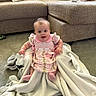 Hazel is registered to the contest to win money with this photo: baby, child, pink_dress, blanket, carpet, couch, pillow, indoor, smiling, cute, sitting, person, floor, soft_texture, home, infant, happy, comfortable, young_child, playful