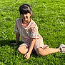 child, girl, grass, outdoor, sunlight, casual, pink_clothing, shorts, tshirt, sneakers, smile, fringe_hair, nature, relaxing, greenery, daylight, portrait, kneeling, park, young