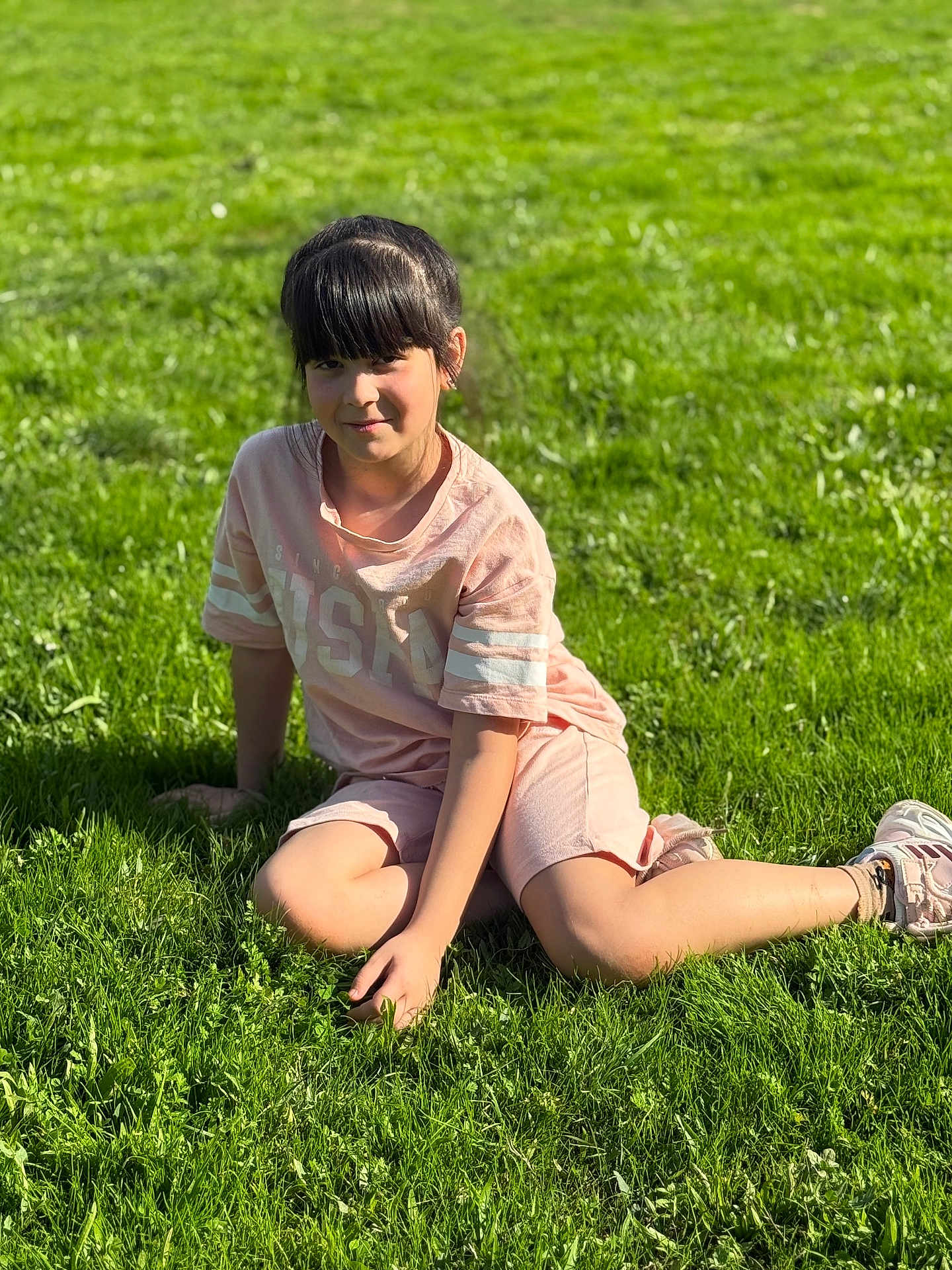 Alfiya participe au concours pour gagner de l'argent avec cette photo : child, girl, grass, outdoor, sunlight, casual, pink_clothing, shorts, tshirt, sneakers, smile, fringe_hair, nature, relaxing, greenery, daylight, portrait, kneeling, park, young
