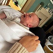 Lorenzo is registered to the contest to win money with this photo: baby, infant, blanket, hand, sleeve, knitted, smiling, happy, person, indoor, home, furniture, wooden_floor, cozy, child, newborn, portrait, care, comfort, warm