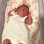 Kori is registered to the contest to win money with this photo: baby, sleeping, infant, white_dress, headband, bow, blanket, floral_pattern, bassinet, sock, rest, peaceful, cute, newborn, child, indoors, soft_lighting, portrait, cozy, fabric