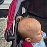baby, child, stroller, red_canopy, blond_hair, curl, cartoon_shirt, outdoor, gravel, side_profile, infant, seatbelt, black_stroller_frame, curious, young_child, casual_clothing, daylight, head, face, person