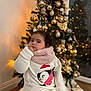 child, christmas_tree, curly_hair, cute, decor, festive, golden_balls, holiday, indoor, lights, ornaments, penguin, scarf, seated, sweater, thoughtful, toddler, warm, white_clothing, winter_clothing