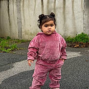 Ayla participe au concours pour gagner de l'argent avec cette photo : toddler, child, outdoor, pavement, pink_clothing, velour_tracksuit, shoes, concrete_wall, greenery, casual, portrait, standing, curly_hair, two_buns, expression, fashion, urban, sidewalk, cute, young_child