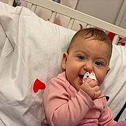 Aryana-Maria participe au concours pour gagner de l'argent avec cette photo : baby, infant, pacifier, pink_clothing, crib, white_bedding, red_hearts, earrings, smile, happy, child, indoor, cute, portrait, person, baby_toy, head, face, sitting, cozy