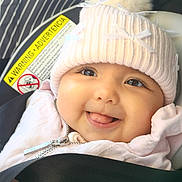 Rylann is registered to the contest to win money with this photo: baby, infant, child, smiling, tongue_out, portrait, close_up, winter_clothing, knit_hat, pom_pom, pink_clothing, scarf, car_seat, seat_belt, vehicle_interior, warning_label, outdoor_travel, face, happy, photography