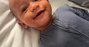 Theodore is registered to the contest to win money with this photo: baby, bed, child, cozy, cute, expression, face, happy, head, human, indoors, infant, lying_down, pajamas, pillow, portrait, skin, sleepwear, smiling, young_child