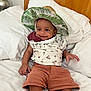 baby, child, smiling, hat, leafy_hat, bed, pillow, white_bedspread, shorts, tropical_print, indoor, cute, happy, infant, person, portrait, relaxed, clothing, skin, hand