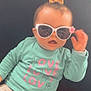 baby, child, sunglasses, bow, shirt, love, sign_language, mint_green, pink, white, pants, couch, pillow, indoor, cute, smiling, hand, face, fashion, seated