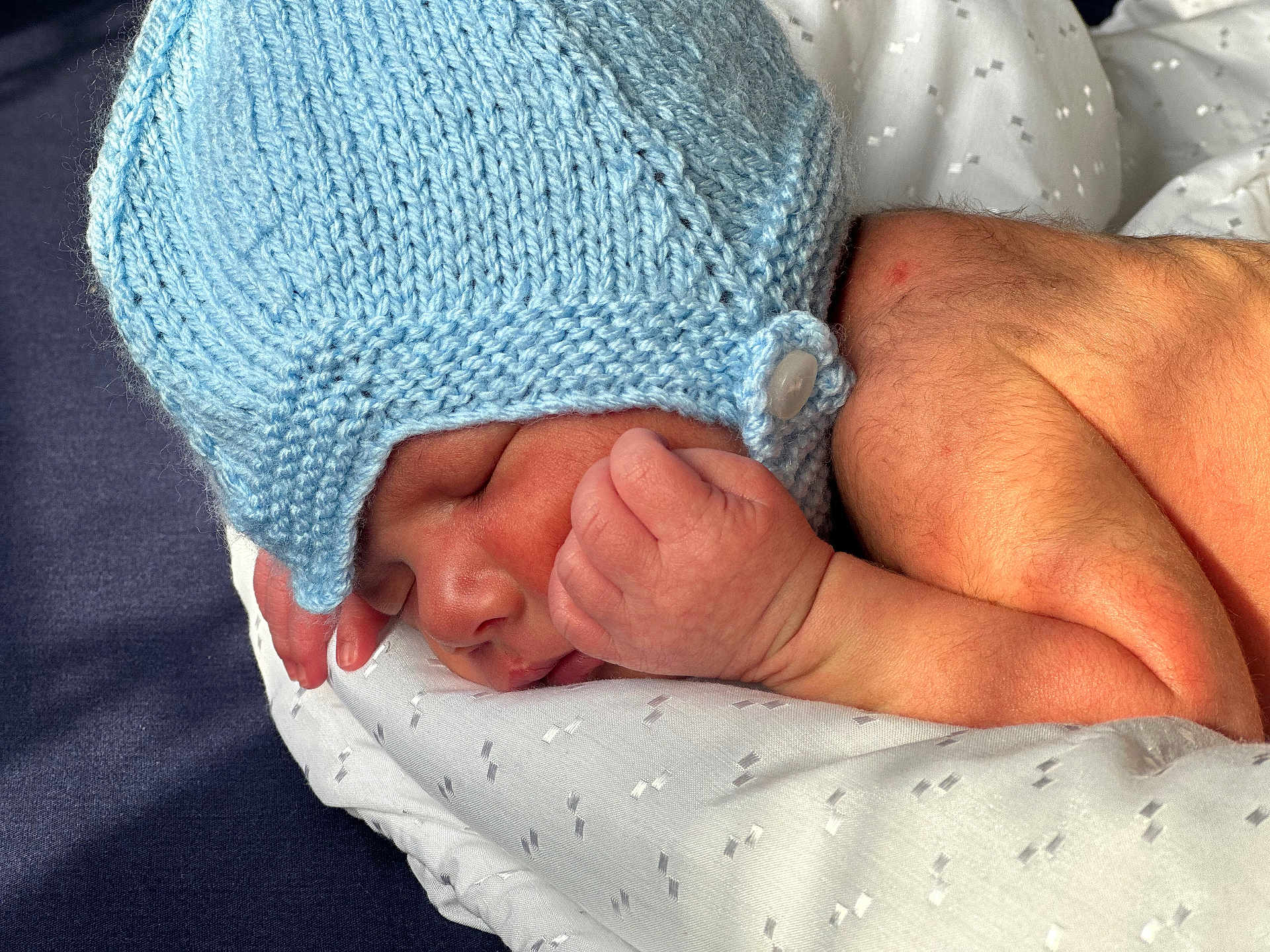 Aarvik joined the competition — help win amazing prizes! newborn, baby, sleeping, blue_hat, knit_hat, hand, blanket, closeup, infant, soft, peaceful, resting, skin, adult_hand, cozy, portrait, indoor, cute, tender, warmth