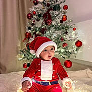 Joud participe au concours pour gagner de l'argent avec cette photo : baby, child, santa_claus_costume, christmas_tree, holiday, festive, lights, ornaments, red_clothing, hat, blanket, indoors, decorations, celebration, cute, smiling, seasonal, warm, cozy, portrait
